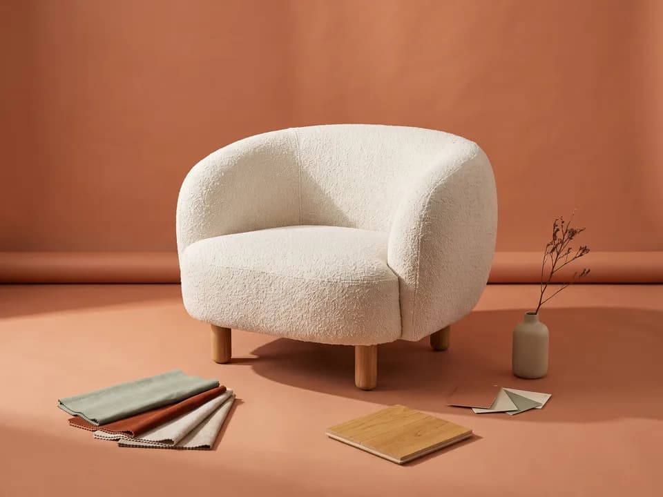 A cream bouclé armchair on terracotta, with fabric swatches, an oak flooring sample and paint chips at its feet